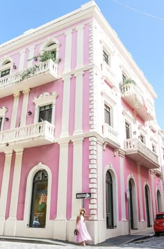 a woman standing in front of a pink and white building