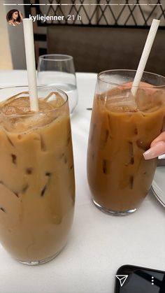 two glasses filled with iced coffee sitting on top of a table next to each other