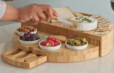 a person is cutting cheese on a board with olives, tomatoes and crackers