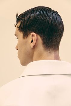 a man with black hair wearing a white shirt and looking off to the side in profile