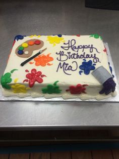 a birthday cake decorated with paintbrushes and acrylic colors on a table