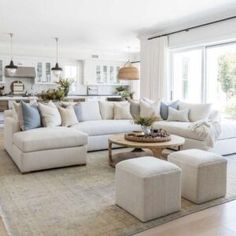 a living room filled with white furniture and lots of pillows on the couches in front of large windows