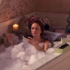 a woman sitting in a bathtub filled with foamy bubbles next to a candle