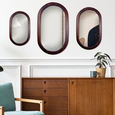 three oval mirrors mounted on the wall above a dresser in a room with a blue chair