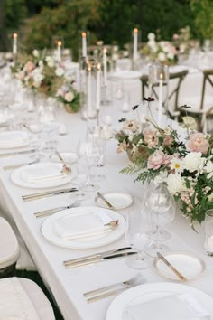 a long table is set with white plates and silverware for an elegant wedding reception