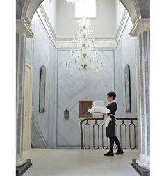 a woman is walking down the hall with towels in her hand and a chandelier hanging from the ceiling