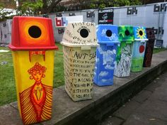 several brightly colored trash cans lined up on the sidewalk