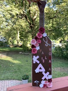 a wooden sign with flowers on it sitting in front of a tree and some grass