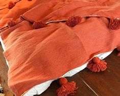 an orange blanket with pom - poms on it is laying on the floor