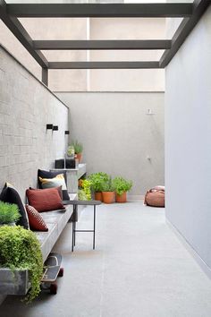 an outdoor patio with benches and potted plants on the side walk, next to a concrete wall