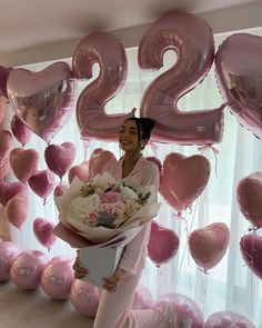 a woman holding a bouquet of flowers and balloons in front of a number twenty sign