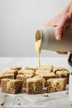 someone pouring sauce onto some food on top of a sheet of wax paper next to a cup