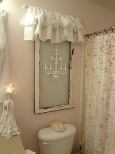 a white toilet sitting in a bathroom next to a shower curtain and window with a chandelier