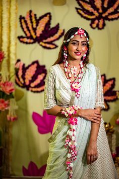 a woman standing in front of a wall with flowers and garlands around her neck