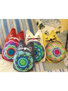 three crocheted cats sitting on top of a couch next to pillows and blankets