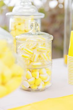 yellow and white candies are in glass containers on a table with other desserts