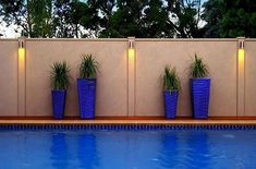 three tall blue vases with plants in them next to a swimming pool and fence