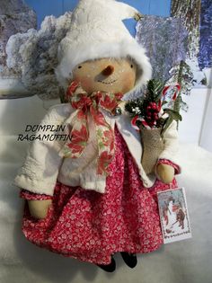 an old fashioned doll wearing a white hat and red dress holding a christmas tree ornament