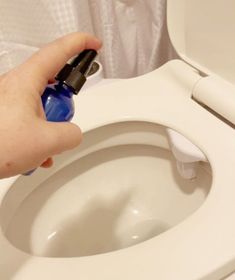 a person is cleaning a white toilet with a blue sprayer on the seat and lid