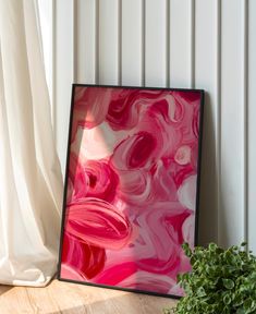 a pink and white painting sitting on top of a wooden floor next to a plant