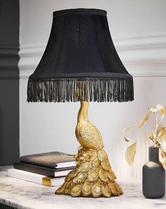 a gold peacock lamp sitting on top of a table next to a vase with flowers