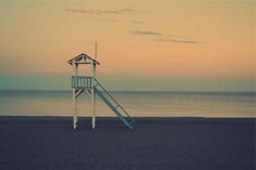 a lifeguard tower sitting on top of a beach next to the ocean at sunset