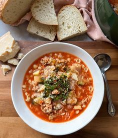 a white bowl filled with soup next to sliced bread on top of a cutting board