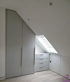 an attic bedroom with white walls and drawers