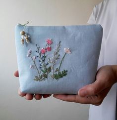 a person is holding a small pouch with embroidered flowers on the front and back side