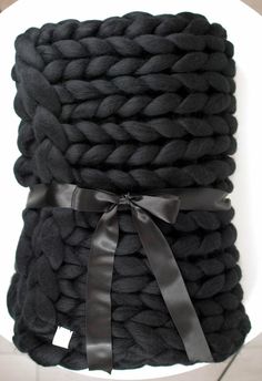 a pile of black knitted blankets on top of a white table with a ribbon tied around it