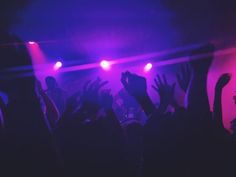 a crowd of people at a concert with their hands in the air and lights on