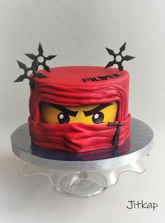 a red cake with black stars on top and a ninja face on the side that has been made to look like a lego head