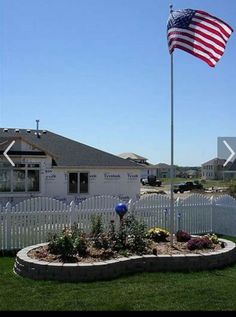 an american flag is flying in front of a white picket fenced yard and house