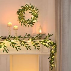 a mantel decorated with greenery and lit candles in front of a fireplace mantle