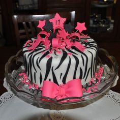 a zebra print cake with pink bows and stars on top is sitting on a glass platter