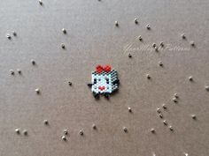 a hello kitty beaded brooch sitting on top of a table next to silver balls