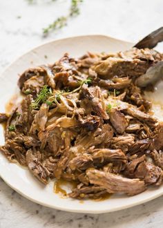 a white plate topped with meat and gravy on top of a marble counter