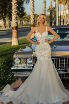 a woman standing in front of a car wearing a wedding dress with an open back