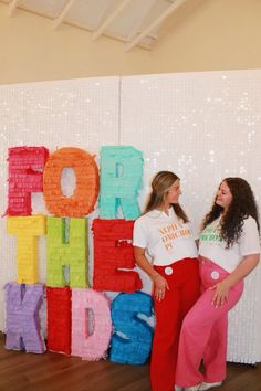 two women standing next to each other in front of letters