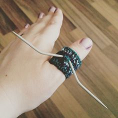 a woman's hand holding a crocheted bracelet with two white sticks sticking out of it