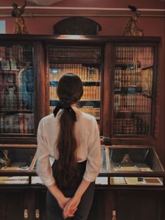 a woman with long hair standing in front of a display case filled with books and other items