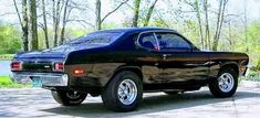 an old black car is parked on the side of the road in front of some trees