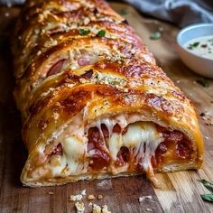 a cheesy pizza is cut in half on a wooden cutting board next to a bowl of sauce