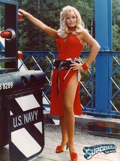 a woman in a red dress is standing on a dock with her arms out and pointing at something