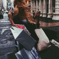 a woman is walking down the street with her hair blowing in the wind and holding shopping bags