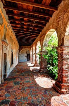 an old building with brick pillars and arches on the outside, along with green plants