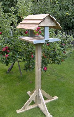 a bird feeder in the middle of some grass with apples growing on it's roof