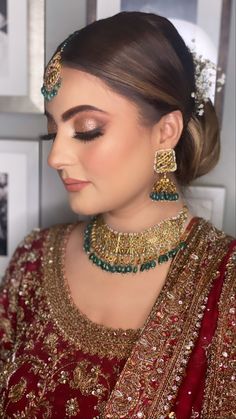 a woman wearing a red and gold bridal outfit with green jewelry on her head