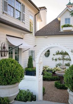 a white house with an arch in the middle and some bushes around it on either side