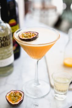 an orange cocktail in a martini glass on a marble table with two glasses next to it